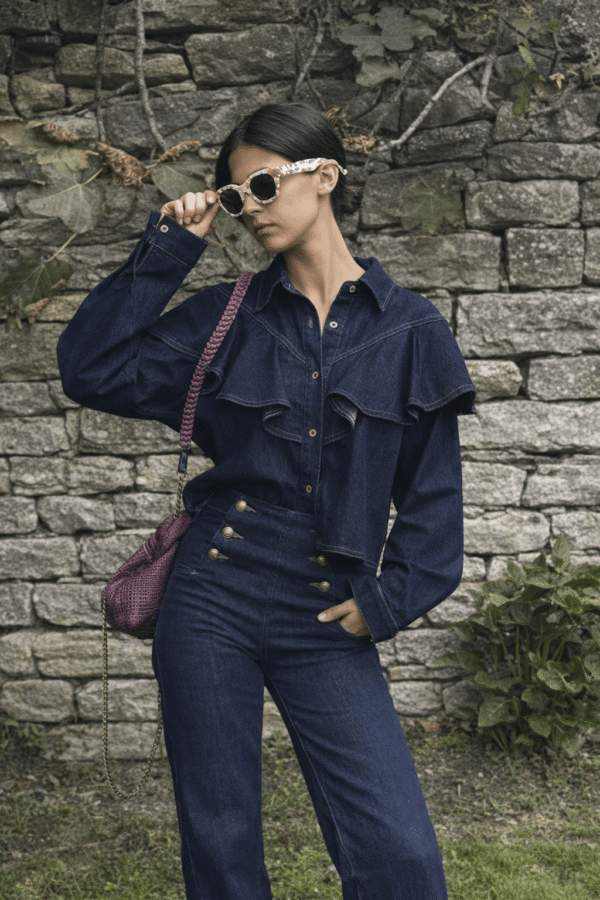 Camisa denim volantes azul oscuro con pantalón vaquero de botones, junto a un muro de piedra