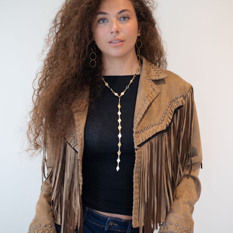 Chaqueta de ante camel con flecos y tachuelas sobre top negro y vaqueros