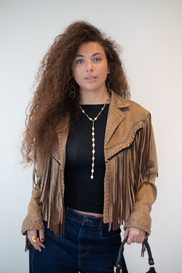 Chaqueta de ante camel con flecos y tachuelas sobre top negro y vaqueros