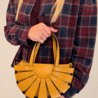 Bolso Abanico Soleil de piel italiana en mostaza, en la mano sobre camisa de cuadros