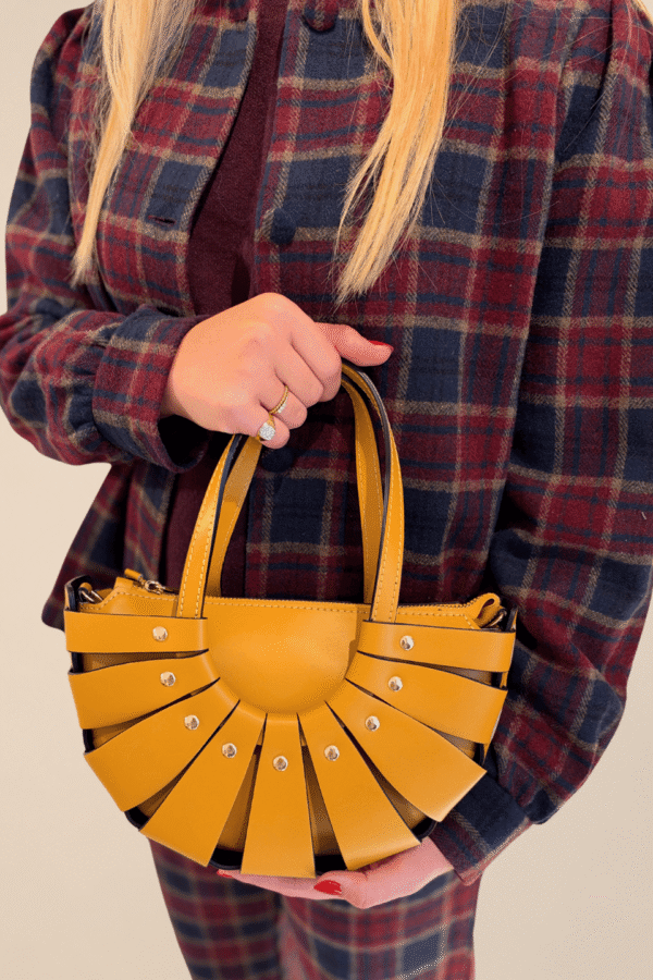 Bolso Abanico Soleil de piel italiana en mostaza, en la mano sobre camisa de cuadros