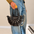 Bolso Abanico Soleil negro con cadena dorada llevado de la mano con vaqueros