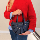 Bolso Abanico Soleil azul marino de piel con remaches dorados, llevado al brazo