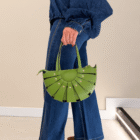 Bolso Abanico Soleil verde pistacho colgado de la mano con vaqueros acampanados