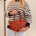 Bolso Abanico Soleil teja sujeto con las dos manos sobre jersey de rayas