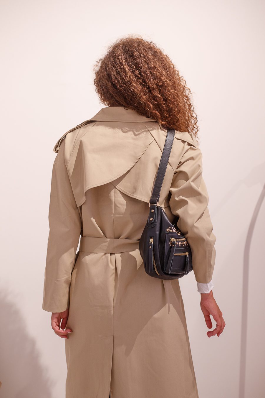 Espalda de la gabardina Amulet beige con canesú y bolso negro al hombro