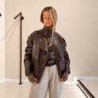 Chaqueta Biker marrón de polipiel con cuello alto, sobre camisa de cuadros y pantalón gris