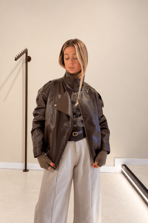 Chaqueta Biker marrón de polipiel con cuello alto, sobre camisa de cuadros y pantalón gris